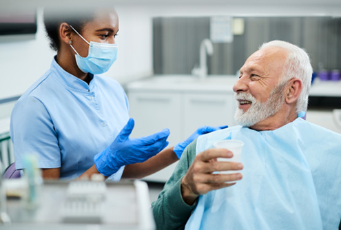 Senior male dental patient talking to dental team member with mask