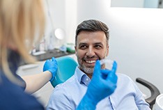 Man in blue striped collared shirt sitting in dental chair with dentist in blue gloves holding Invisalign