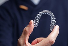 Dentist in blue scrubs holding up Invisalign tray