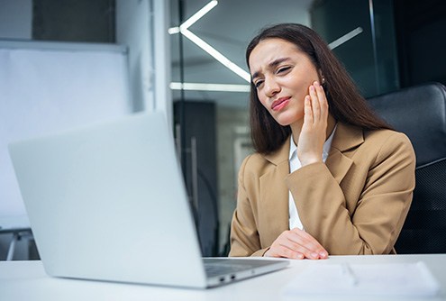 Woman at laptop rubbing her jaw and looking concerned